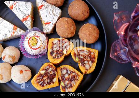 Assorted Indian sweets or Mithai, Rava laddoo, Besan laddu, dry fruits sweets in a black plate along with Happy Diwali chocolates for Diwali festival. Stock Photo