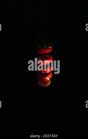 Sliced red tomato in the air on a black background, vertical distance shot. High quality photo Stock Photo