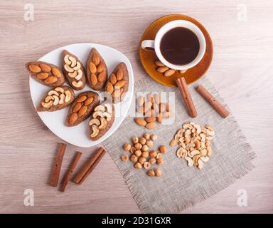 Small cakes "potatoes" with almonds and cashew nuts on a dessert plate. A cup of coffee, cinnamon, almonds, hazelnuts, cashew on a linen napkin. Still Stock Photo
