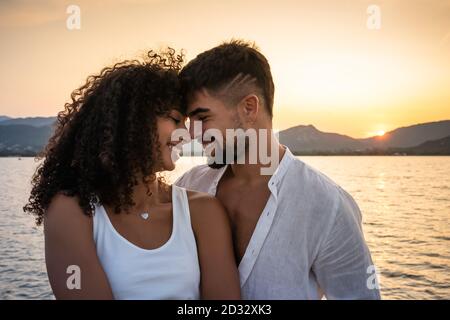 Happy mixed race couple, Caucasian attractive bearded man with her cute Hispanic girlfriend, smiling face to face looking each other with setting sun Stock Photo