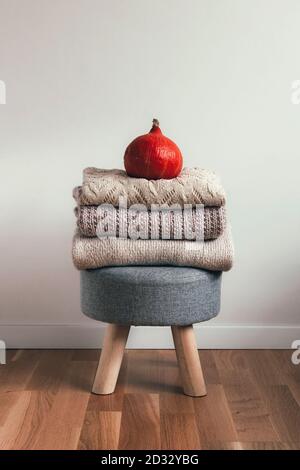 A stack of folded sweaters on a stool and orange pumpkin on top. Autumn mood concept. Stock Photo