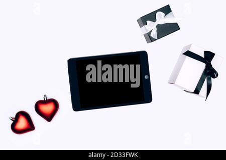 Black and white gift boxes, heart shaped Christmass tree baubles and electonic tablet on white background. Flat lay composition for birthday, Christmas, wedding. Online shopping concept. Stock Photo