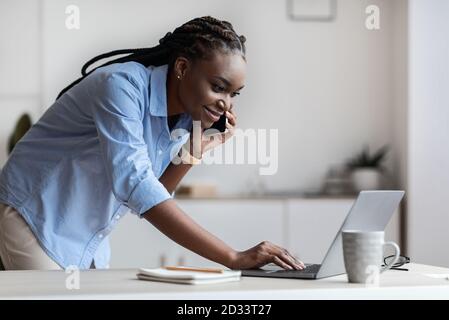 Female Entrepreneur. Smiling African Businesswoman Talking On Phone And Working On Laptop Stock Photo