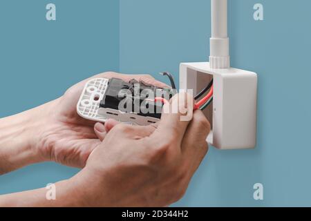 Closeup hands of electrician plugs the power cord into the wall outlet isolated on pastel color background, with clipping path. Stock Photo