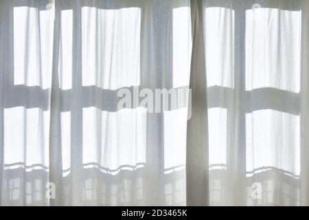 Morning sun shines through white transparent curtains with shadows from the window frame. Stock Photo