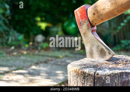 Old steel axe tool with traces of red paint impaled in log. Hatchet tool for splitting wood stumps and chopping logs in a garden. Stock Photo