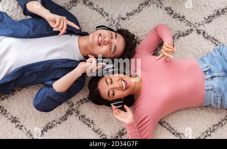 Asian Couple In Headphones Listening Music Lying On Floor Indoors Stock Photo