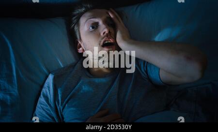 Top View of a Young Man in Bed at Night Having Terrible Nightmare, He Wakes Up Scared and Covered in Sweat. Stock Photo