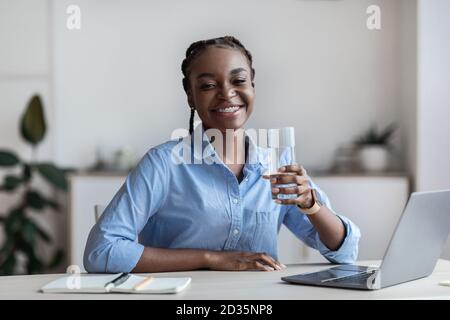 Hydration At Work. Happy Black Female Office Worker Holding Glass Of Water Stock Photo