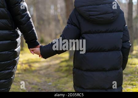 Mother and daughter holding hands while walking in the forest. Happy family hiking and spending time outdoors in nature Stock Photo