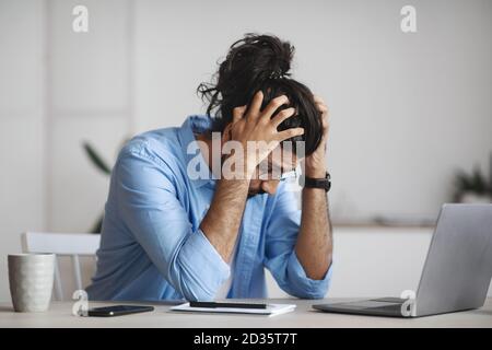 Work Problems. Desperate indian manager sitting at desk in office, suffering from business failure Stock Photo