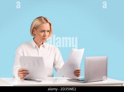 Focused business lady working with documents near laptop computer at her desk against blue background, copy space Stock Photo