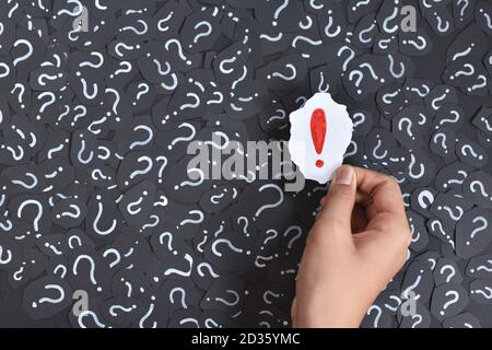 Hand holding an Exclamation Mark against Question Mark backgrounds. Concept of FAQ, Q&A and Answers Stock Photo