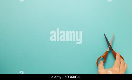 Scissors with hand on blue background. top view, copy space Stock Photo