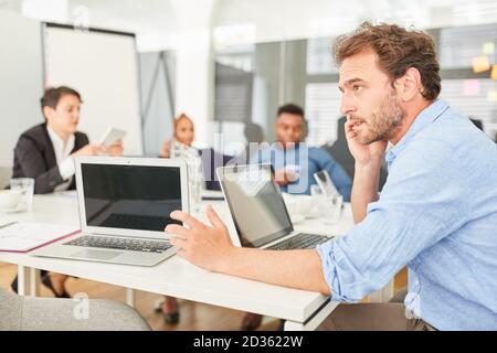 Business man working on laptop computer in office in meeting talking on mobile phone Stock Photo