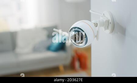 Close Up Object Shot of a Modern Wi-Fi Surveillance Camera with Two Antennas on a White Wall in a Cozy Apartment. Man is Sitting on a Sofa in the Stock Photo