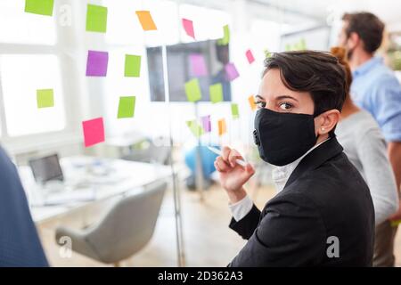 Business woman with mask because of Covid-19 and coronavirus in the brainstorming workshop Stock Photo