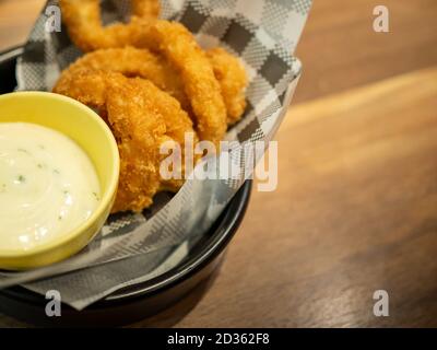 Fish fingers and mayonnaise sauce are on a black plate and on a brown wooden table. Stock Photo