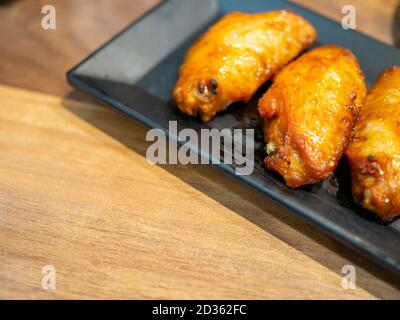 BBQ chicken wings on a black plate and placed on a brown wooden table with copy space. Stock Photo