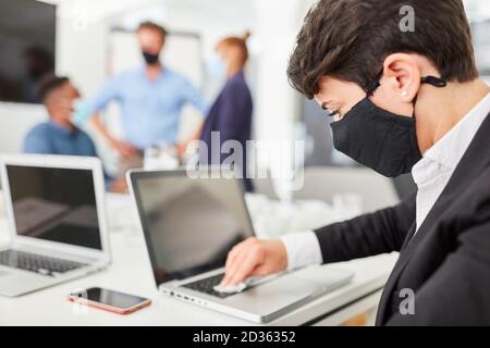 Young businessman with face mask disinfecting the PC keyboard Stock Photo