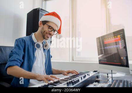 Merry Christmas and a happy new year Composer hands on piano keys in recording studio. music production technology, man in christmas hat is working on Stock Photo