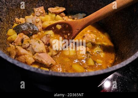 Ragout of potatoes and meat in a saucepan on the stove. A large wooden spoon mixes the lamb stew. Preparation of dishes from potatoes with broth and B