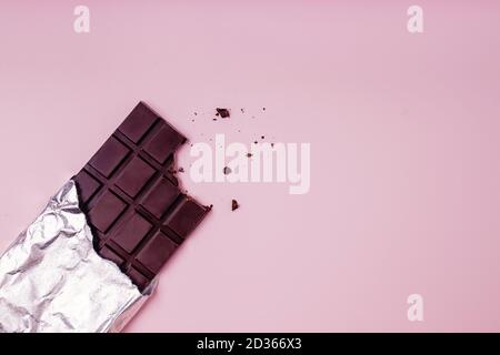 Bited bar of chocolate in foil with crumbs on pink background. Copy space Stock Photo