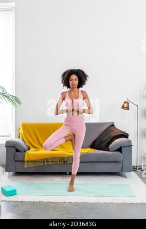 Afroamerican woman practicing yoga tree pose at cozy home Stock Photo