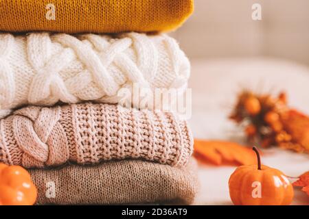 A stack of knitted things in the autumn decoration of pumpkins and yellow leaves. Stock Photo