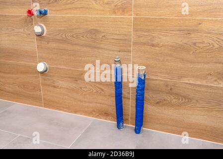 Pipes with water coming out of the floor and from the wall and sewer pipes in the wall in a modern boiler room lined with brown ceramic tiles. Stock Photo