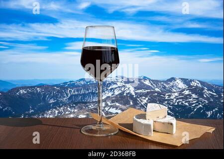 Glass of red wine against mountains background. Closeup view of glass of red wine over snowy mountains. Stock Photo