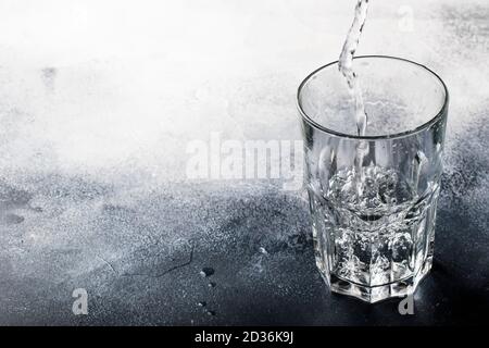 Clear water is poured from glass bottle into glass, gray background, selective focus Stock Photo