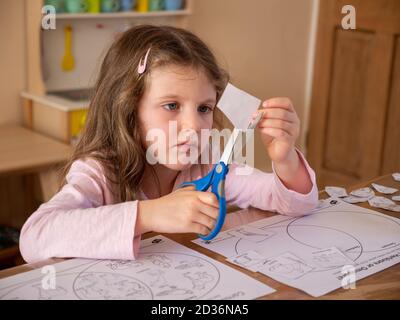 Young six year old girl using scissors to cut pictures on paper for her school homework at home, UK Stock Photo
