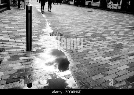 Two People Walking In The Distance On A pavement With Standing Water Puddles Reflection of Clouds in the Sky Stock Photo