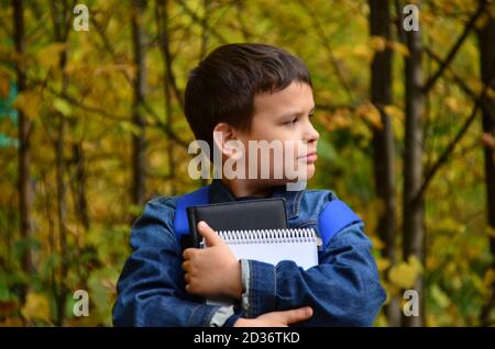 Serious teenage boy with laptop and textbooks doing homework and preparing for the exam in the park among the trees. The concept of heavy learning, a Stock Photo