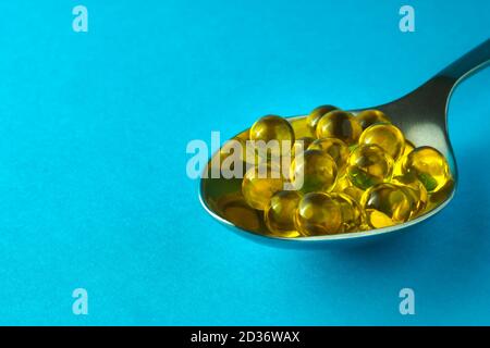 Heap of round fish oil capsules in silver spoon on blue background. Selective focus, copy space Stock Photo