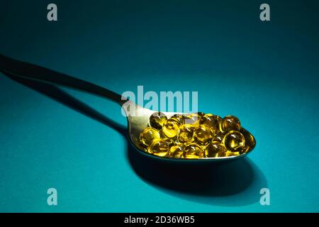 Fish oil capsules in spoon on blue background, selective focus, copy space Stock Photo