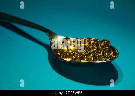 Round fish oil capsules in spoon on blue background, selective focus, close-up Stock Photo