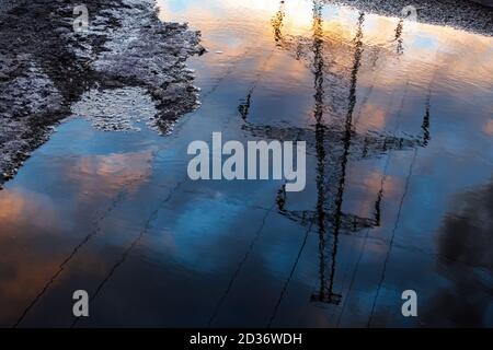 Reflection in puddle of transmission tower on cloudy sky background in springtime, selective focus Stock Photo