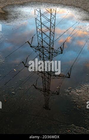 Reflection in puddle of transmission tower on cloudy sky background, vertical view Stock Photo