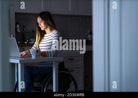 Young woman in wheelchair working on laptop till late Stock Photo