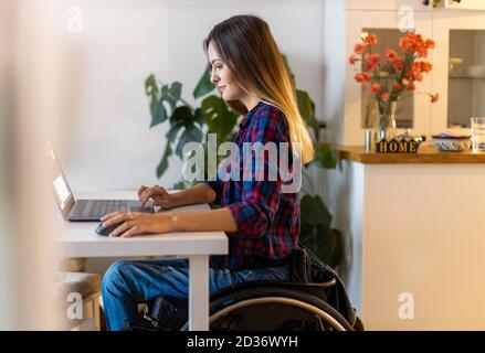 Young woman in wheelchair using laptop at home Stock Photo