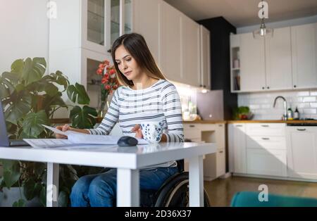 Woman in wheelchair reading documents at her desk at home Stock Photo