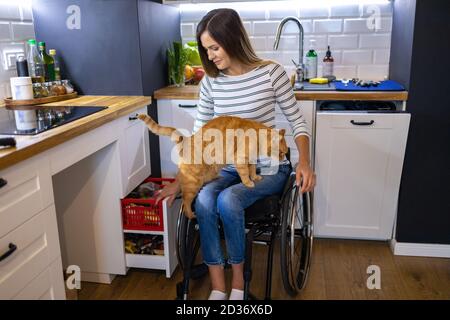 Disabled young woman in kitchen with cat on her lap Stock Photo