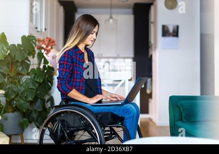 Young woman in wheelchair using laptop at home Stock Photo