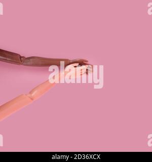 Two doll hands reach for each other on pink background. Different skin tones and races. Stop racism, diversity and unity, equality and feminism Stock Photo