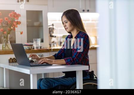 Young woman in wheelchair using laptop at home Stock Photo