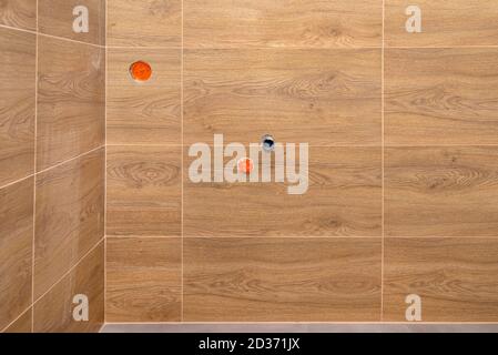 Water pipe and a sewer pipe coming out of a wall in a modern boiler room lined with brown ceramic tiles, visible power socket. Stock Photo