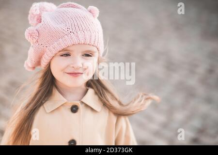 Cute baby girl 3-4 year old wearing knitted hat and beige coat in park outdoors close up. Childhood. Autumn season. Stock Photo