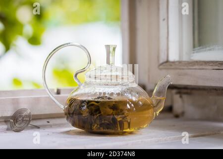 Green tea in a glass teapot on window sill, rustic background, toned Stock Photo